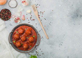 Traditional spicy meatballs in tomato sauce with pepper, garlic and parsley on light table with utensils