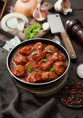 Traditional spicy meatballs in tomato sauce with pepper, garlic and parsley with onion and cleaver on black