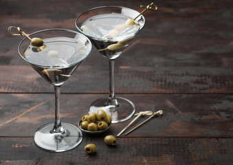 Vodka martini gin cocktail in original glasses with olives in metal bowl and bamboo sticks on wooden board.