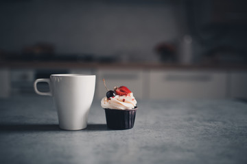 Cup of tea with creamy cupcake with berries staying on kitchen table closeup. Good morning....
