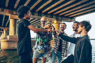 Group of friends celebrating, resting, having fun and party in summer day. Young men drinking beer, talking, laughting. Look happy and cheerful. Festive time, holiday, summertime, unity and friendship