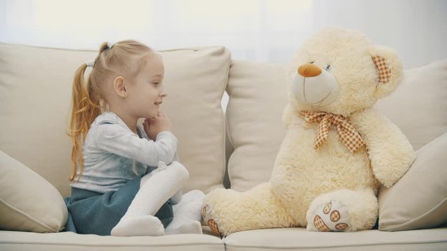 4k video of cute little girl sitting on the sofa, talking with her teddy.