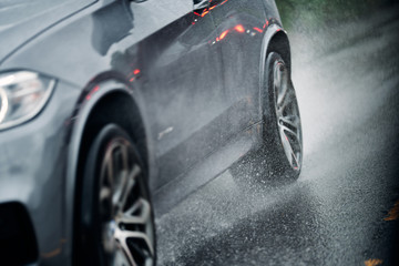 Fototapeta na wymiar Car on wet and slippery asfalt. Close up on tires and the road. Rain and wet driving conditions. 