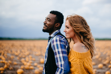 A young woman leaned against her husband's back while standing in a pumpkin field.