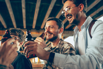 Group of friends celebrating, resting, having fun and party in summer day. Young men drinking beer, talking, laughting. Look happy and cheerful. Festive time, holiday, summertime, unity and friendship
