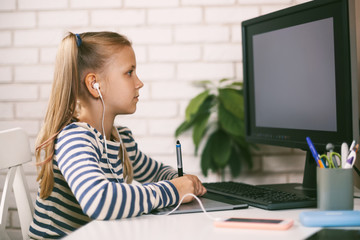 A girl in headphones sits at a table at the computer at home and does her homework Online education. The child learns from home. Distance learning online.