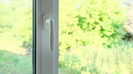 A man closes a white plastic window by the handle.