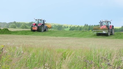 Fototapeta premium Two Tractors collecting silos aon field Close up