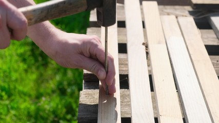 Hammering a big thick nail into wooden board close-up
