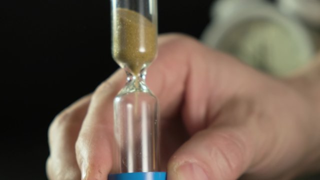 Man's hand flips an hourglass. Close up on black