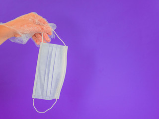 Hand with plastic glove with sanitary mask on violet background with copy space