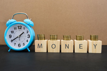 Time is money concept with alarm clock, coins and the word written on wooden cubes. A valuable resource for making money in business. Save time