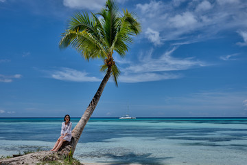 Fototapeta na wymiar Young beautiful girl sitting on palm tree over the Caribbean sea with sunglasses 