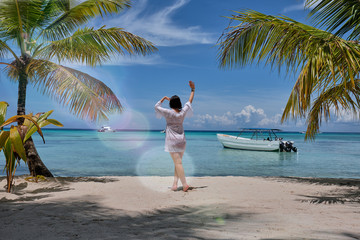 A girl looking horizon standing next to a palm trees on a beach in front of a Caribbean sea 