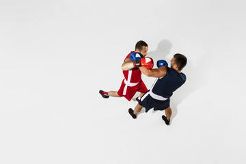 Naklejka na ściany i meble Two professional boxers boxing isolated on white studio background, action, top view. Couple of fit muscular caucasian athletes fighting. Sport, competition, excitement and human emotions concept.