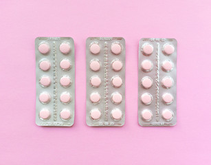 Blisters of soft pink pills on pink background. Monochrome simple flat lay with pastel texture. Medical concept. Stock photo.