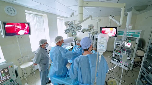 Operation in the hospital. Surgical procedure on modern medical equipment background. Group of surgeons operates patient and look on monitor.