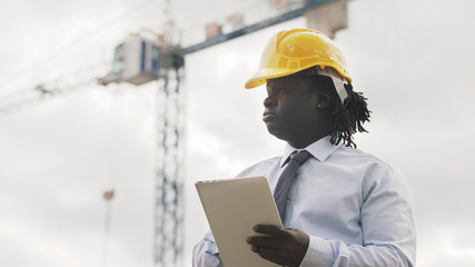 Portrait of an african man with hardhat using tablet on the construction site and observing the work. High quality photo