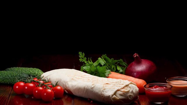 General view of the composition of shawarma and vegetables on a wooden table. Black background.
