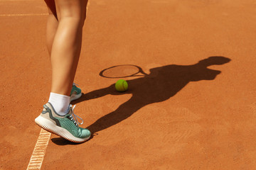 Woman in sneakers on clay court with tennis ball