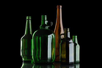 A group of glass bottles on a black isolated background. Transparent alcohol container. Empty container with reflection.