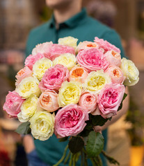 Man with bunch of pink and yellow roses. Young man holding a big bouquet of pink and yellow peonies roses in Women's day. Fresh roses flowers.