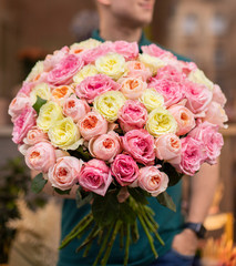 Man with bunch of pink and yellow roses. Young man holding a big bouquet of pink and yellow peonies roses in Women's day. Fresh roses flowers.