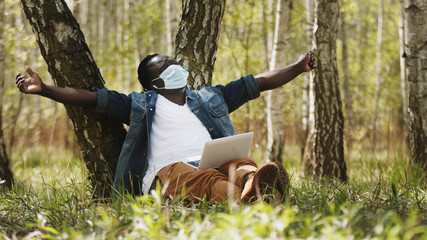 New normal. Remote work concept. African man using laptop in the nature and stretching. High quality photo