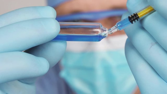 Doctor in medic face mask is preparing an injection. A syringe with a vaccine, medical solute in the hands of the doctor. Close up view