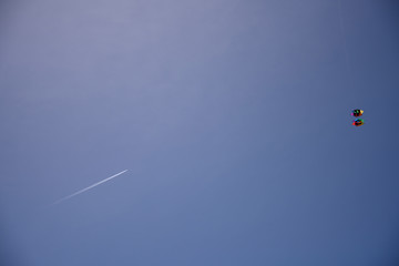 A plane and a kite meet in the blue sky. 