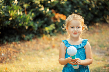 little blonde girl smiles and holds in her hand
soap bubble maker