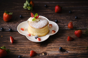 Fluffy souffle pancakes with cream and berries on white plate set on wooden table. - 372974173