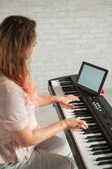 A woman watches video lessons on a digital tablet and plays on an electro synthesizer. The girl learns to play the piano remotely.