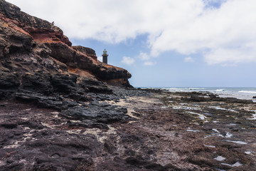 Rocky Atlantic coastline at low tide. In the background, the Punta Jandia lighthouse. Fuerteventura. Canary Islands. Spain.