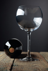 Unopened bottle of red wine and empty wine glass on an old wooden table.