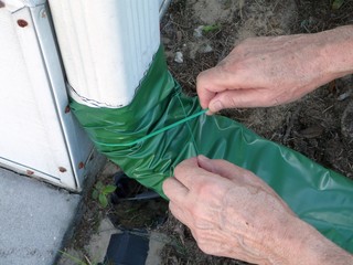 A man is installing an automatic recoiling extender over the gutter downspout that rolls out when it's raining and retracts when it's dry to prevent foundation damage from water.