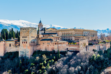Fototapeta na wymiar Alhambra on a hill with some green trees with a snowy mountain in the background, a beautiful sunny day with a blue sky in Granada Spain