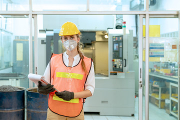 Portrait of female technician engineer control machines in the factory on a business day. Confident worker wearing particulate respirator mask with hard hat. Concept of Industrial manufacturing.