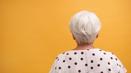 Back view of a senior gray haired woman isolated on the orange background. High quality photo