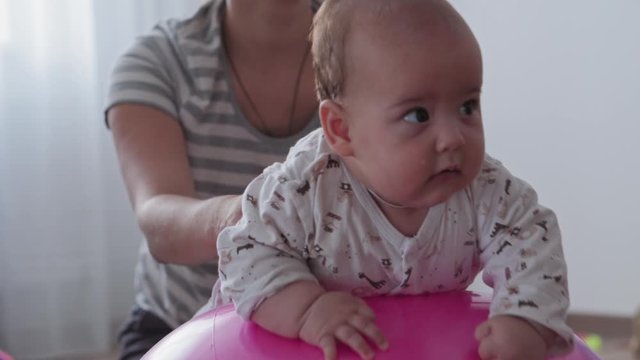 Childhood, Motherhood, games, upbringing and development concept - close-up young mom are joyfully doing exercise and masah with two newborn and little daughters on fitball and smiling in kid playroom