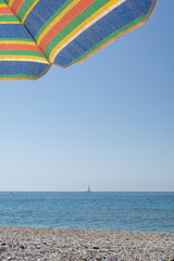 On the beach on a sunny summer day, under a colorful umbrella, looking out to sea where a sailboat sails on the horizon