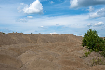 Many small piles of sand and a large sand bank against the sky with clouds.