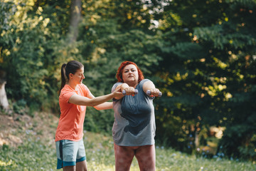 Fototapeta premium An obese woman does weight loss training, arm strengthening exercises, the trainer shows how to do it