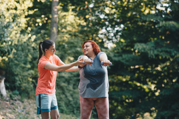 Fototapeta premium An obese woman does weight loss training, arm strengthening exercises, the trainer shows how to do it properly