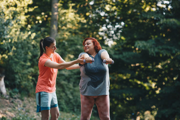 Fototapeta premium An obese woman does weight loss training, arm strengthening exercises, the trainer shows how to do it properly