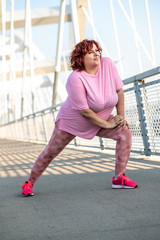 An obese woman does leg stretching exercises on a bridge, preparations for jogging