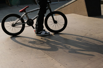 closeup of a young male standing by his bmx bicycle showing only his legs and beautiful shadow on the ground symbolizing youth culture and lifestyle