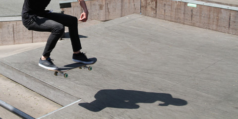 legs of a male youth performing a trick on his skateboard in a skatepark with complete shadow on...