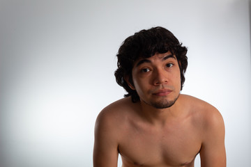 Young nude Hispanic man with wavy hair and shaved beard on a white background, expressing confidence