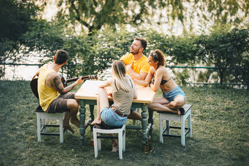 Two couples sit outside in nature, enjoying themselves, eating fast food, drinking beer and smiles